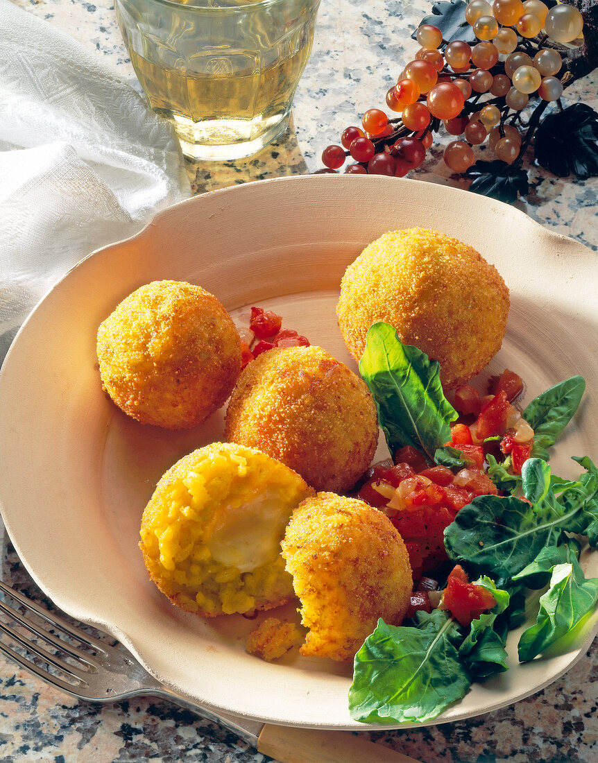 Rice balls with mozzarella, arugula, tomatoes and onions on plate