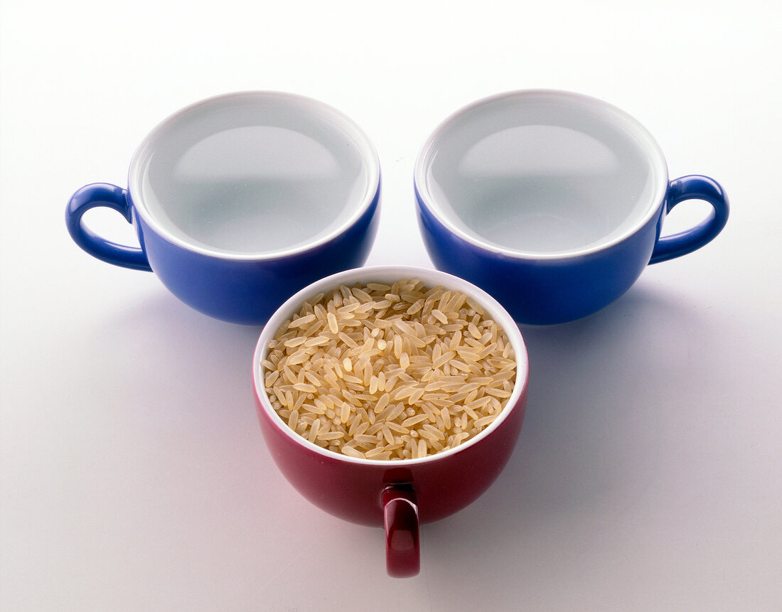 Three cups filled with rice and water on white background