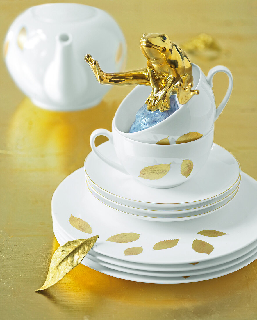 Stack of white plates and cups with golden leaf pattern and frog figure