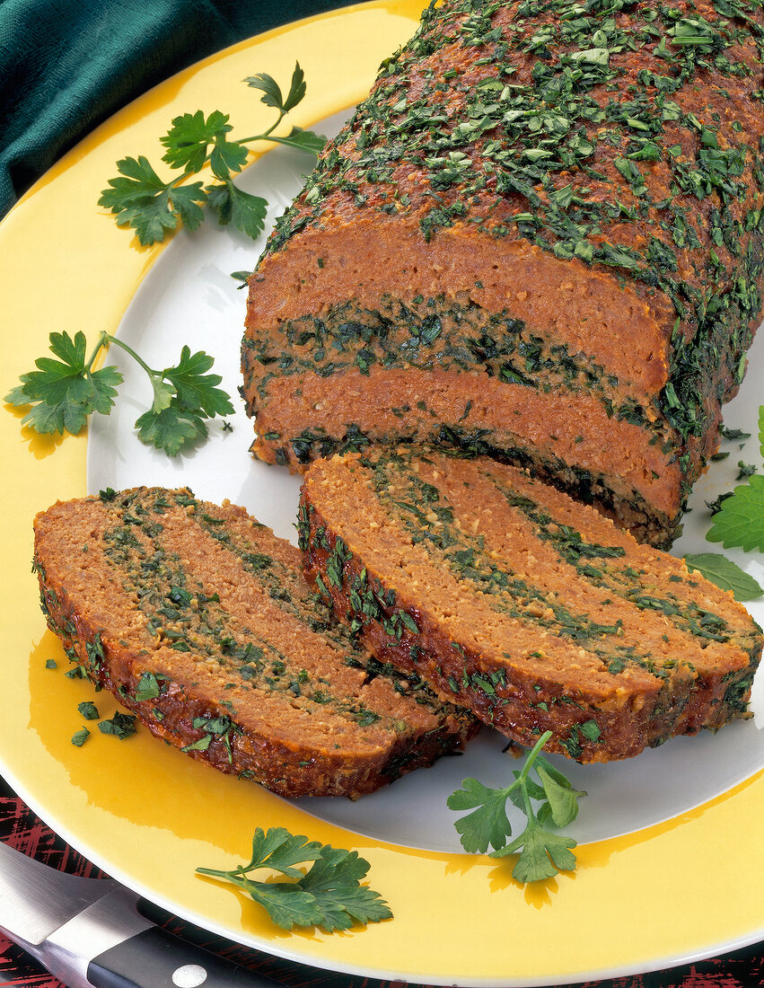 Close-up of sliced brown meatloaf with green herbs on plate