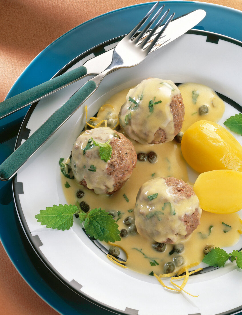 Close-up of meatballs in caper sauce with potatoes and lemon balm on plate