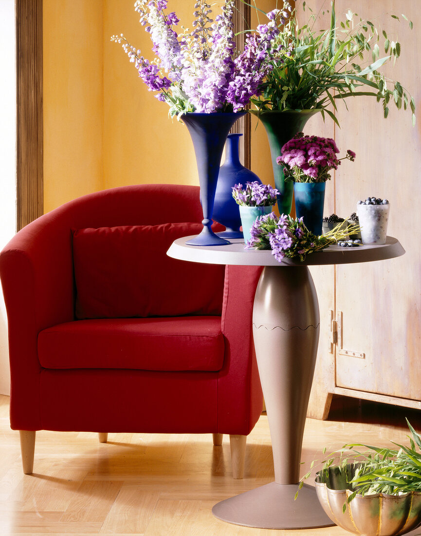 Blumen in Violett in versch. Vasen in Blau, Sessel rot, Tisch rund