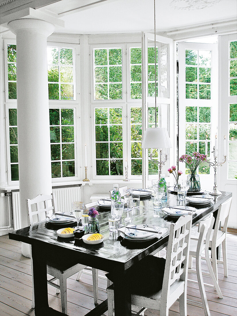 Laid black dining table with white chairs in country style against large window