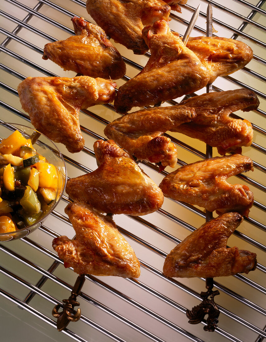 Close-up of chicken wings in skewers and zucchini chutney on grill