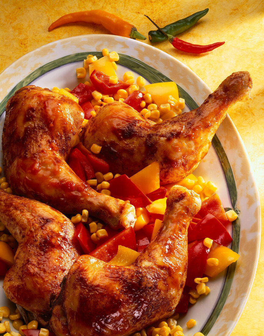 Close-up of chicken legs with corn and peppers on plate