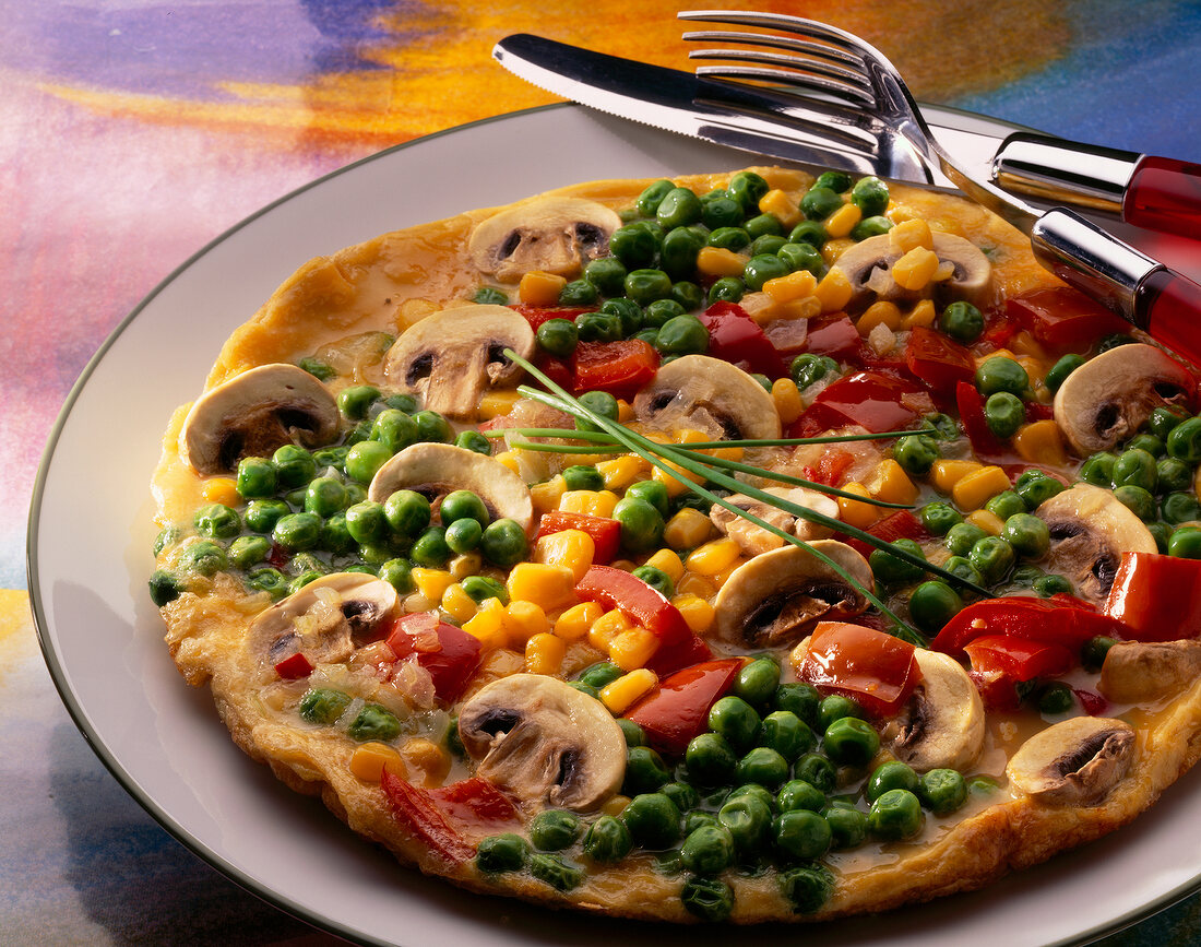 Close-up of vegetable omelette with corn, peas, peppers, mushrooms and chives on plate