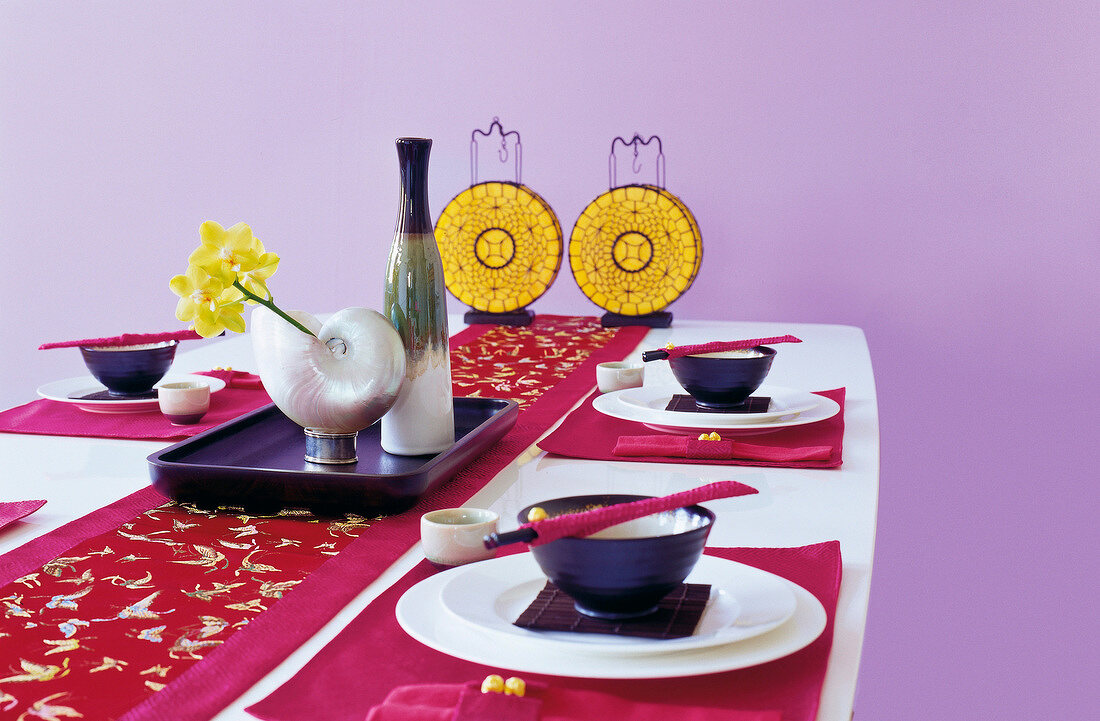 Table laid with Asian tableware, paper lanterns and shell vase with yellow flower