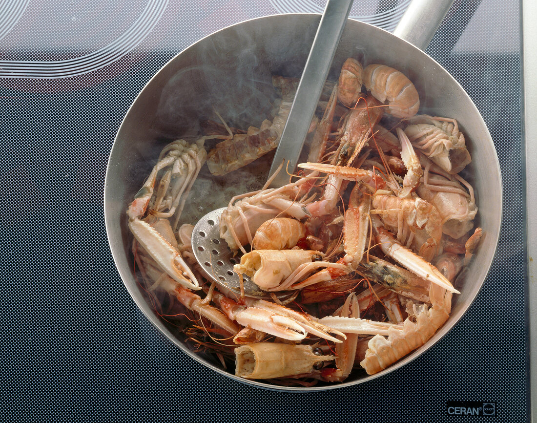 Scampi head, crab legs and other fishes frying in pan with ladle