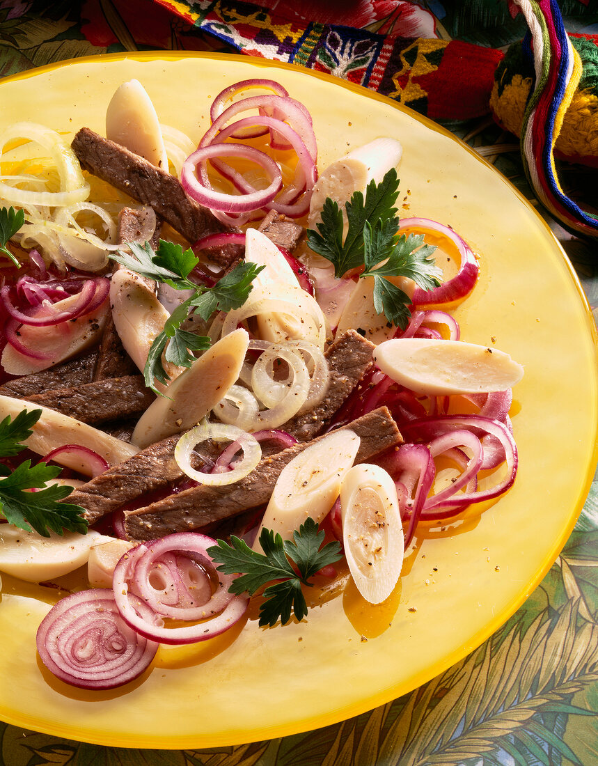 Close-up of Brazilian beef salad with onions and hearts of palm on yellow plate