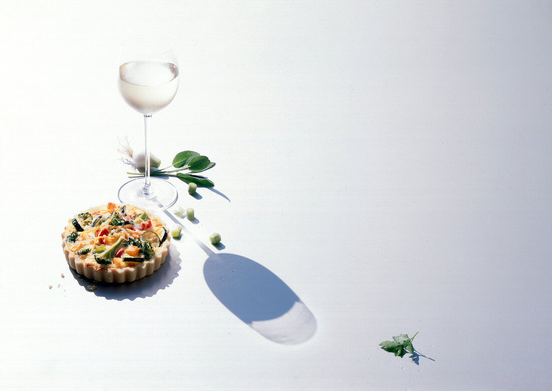 Vegetable quiche with spring onions and white wine glass on white background