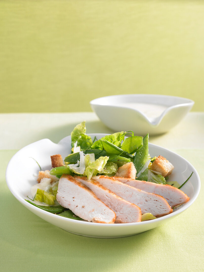 Geflügelsalat mit Zuckerschoten, Croûtons und Parmesan auf Teller