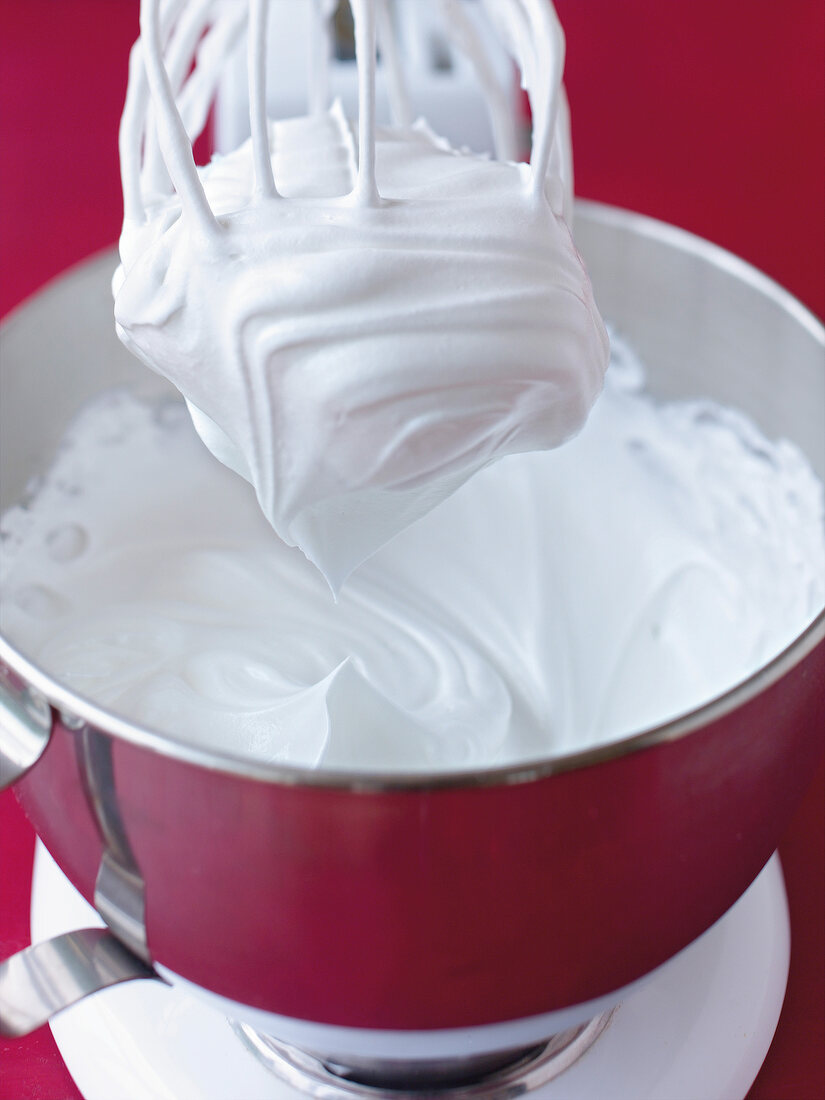 Close-up of meringue whisked with hand mixer in bowl to prepare raspberry pavlova