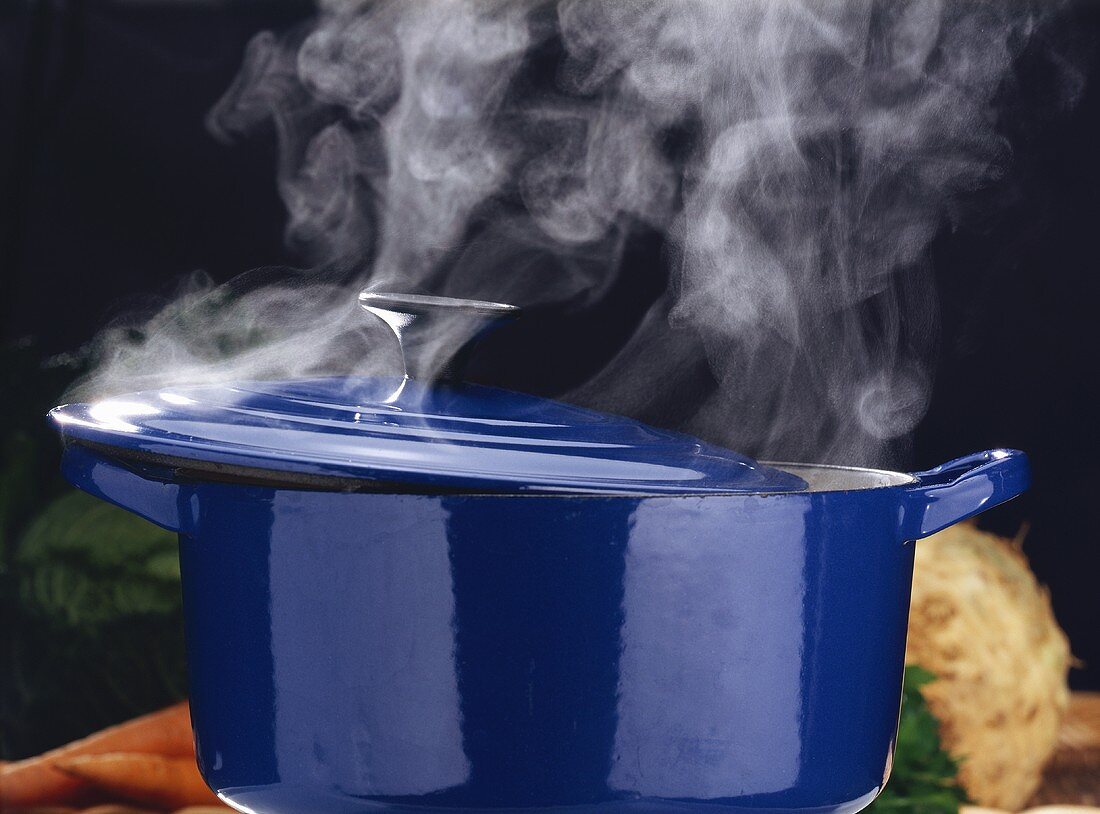 Blauer Kochtopf mit Dampf auf Holztisch; Deckel halb geöffnet
