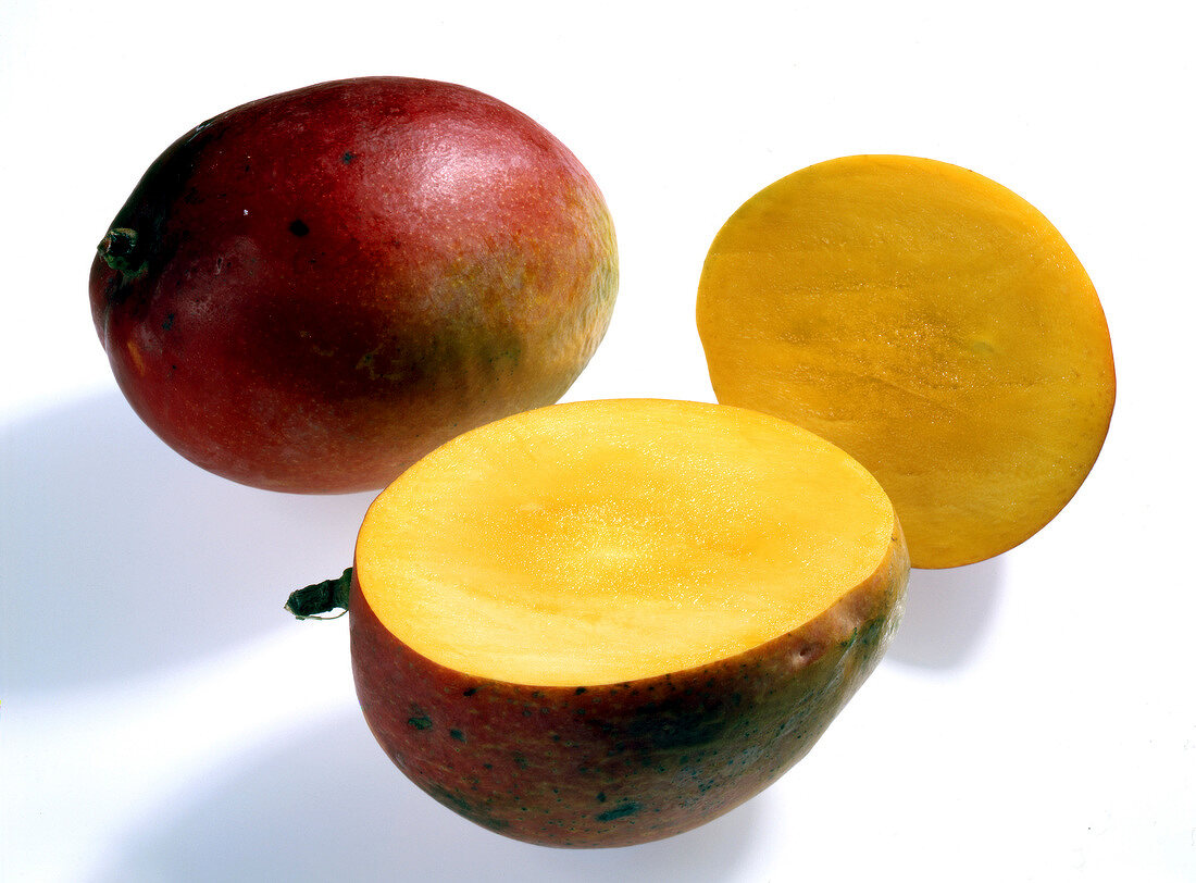 Whole and halved dark red mangoes on white background