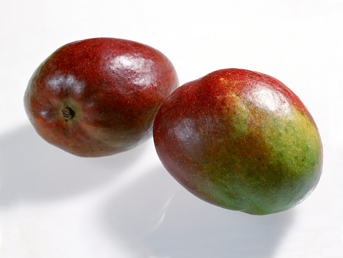 Whole and halved red and green mangoes on white background