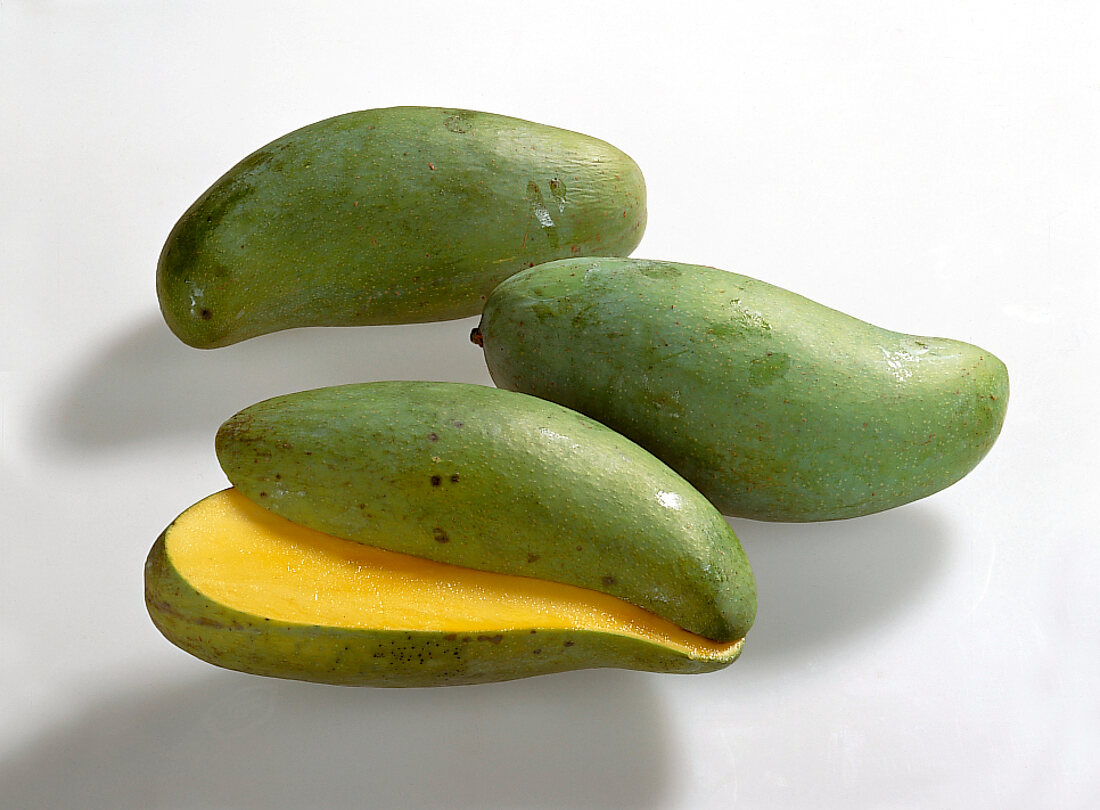 Two whole and halved slender green mangoes on white background