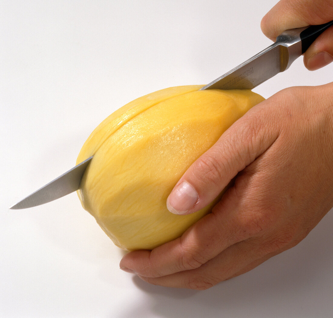 Peeled mango being cut into halves with knife