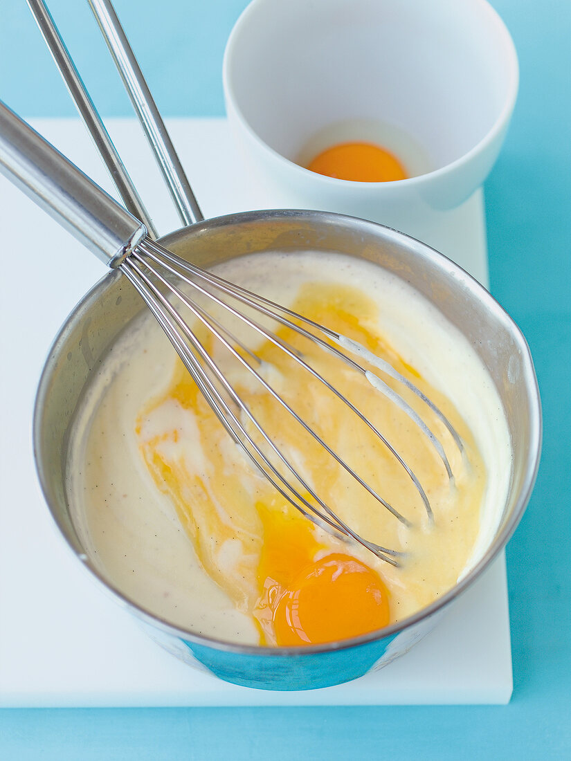 Rührschüssel mit Creme und Schnee- besen, Schale mit Eigelb