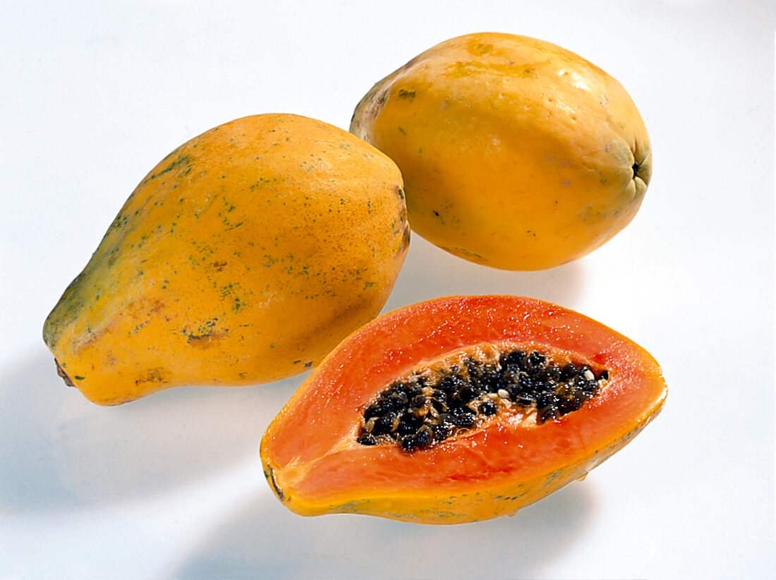 Whole and halved pear shaped papayas with seeds on white background