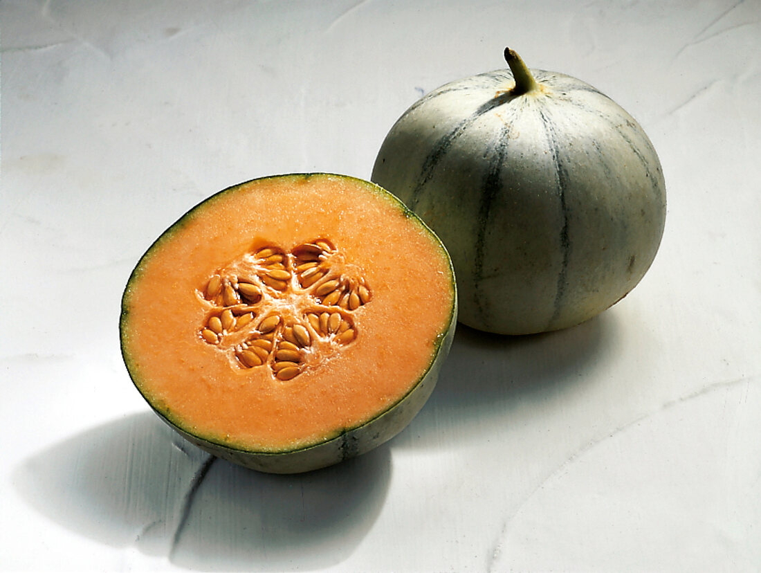 Whole and halved green charentais melon on white surface