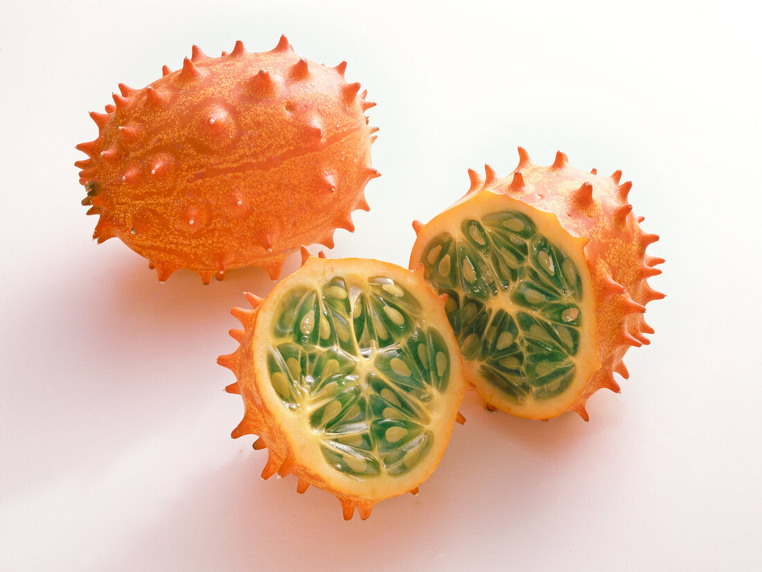 Whole and halved orange horned melon on white background