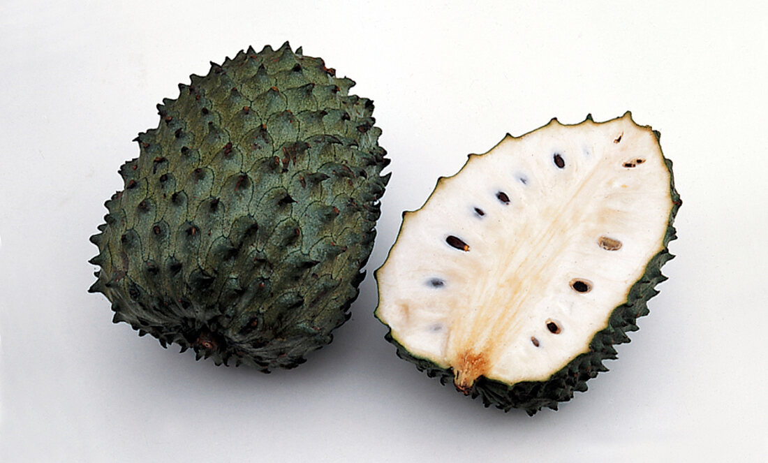 Halved dark green soursop with white flesh on white background