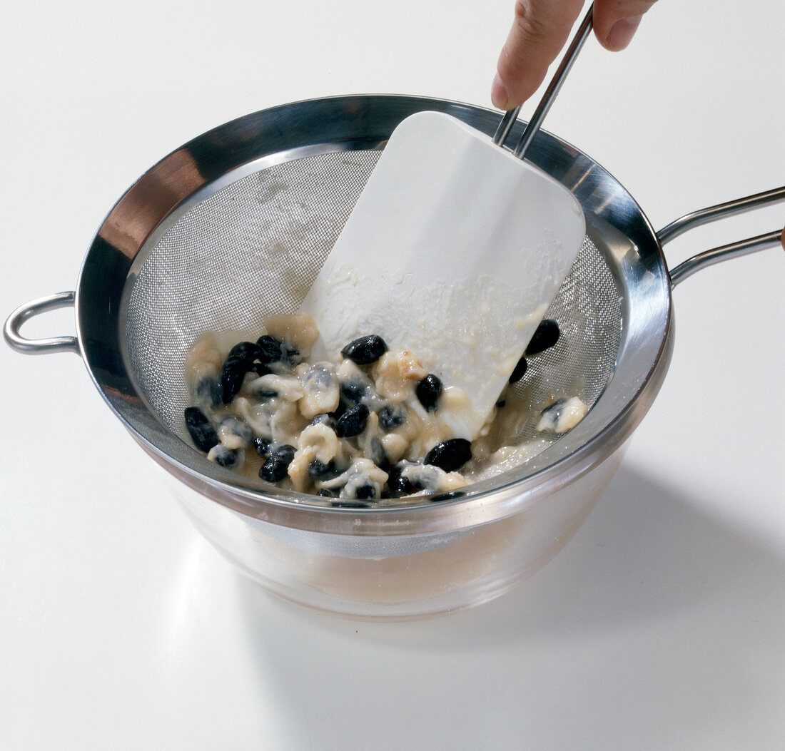 Flesh and seeds of custard apple in sieve with rubber spatula