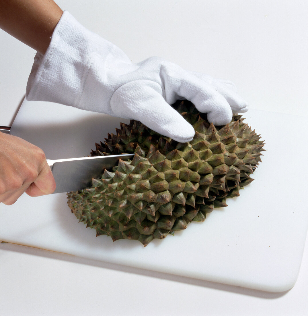 Close-up of man wearing gloves and cutting durian with knife on cutting board