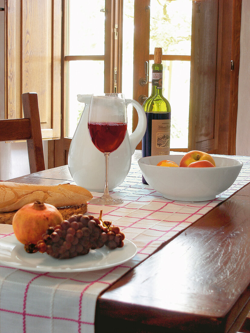 Carafe, fruits and glass of red wine on table in front of window