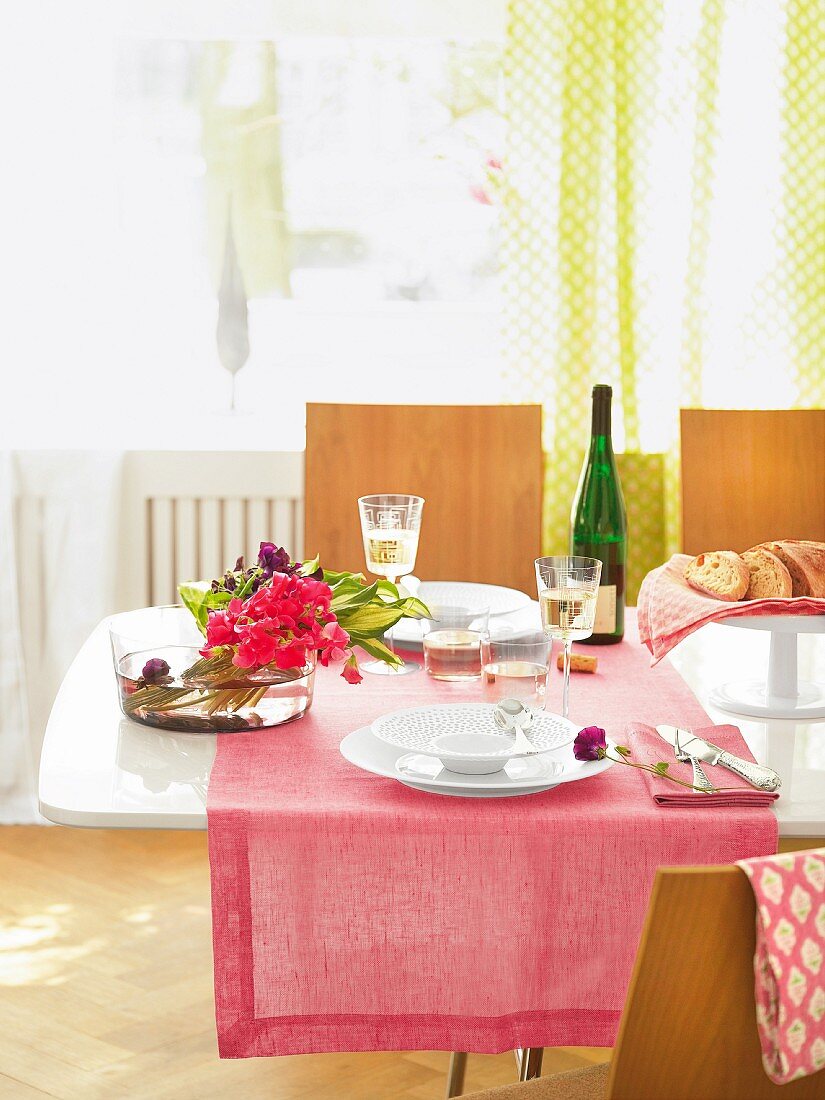 Dining table with pink table cloth, flowers in bowl and white wine