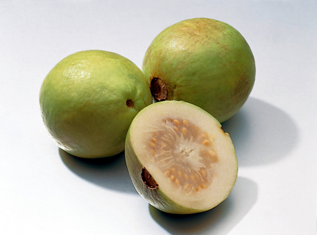 Halved and whole guavas on white background