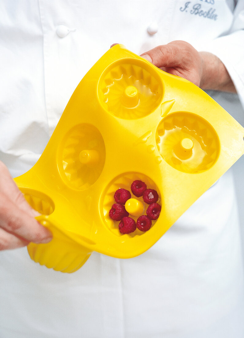 Close-up of chef holding raspberries and gelatin in yellow cake mould