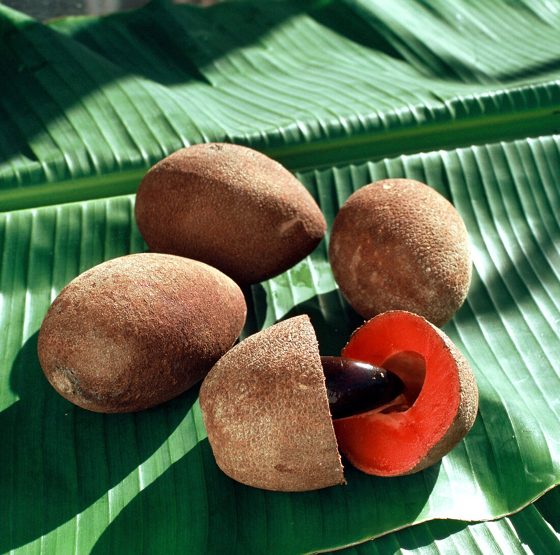 Whole and halved mamey sapote on green leaf