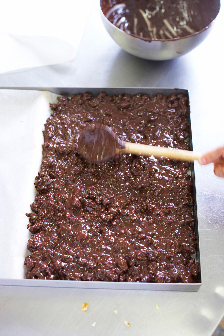 Close-up of chef spreading chocolate mixture on baking sheet with wooden spoon