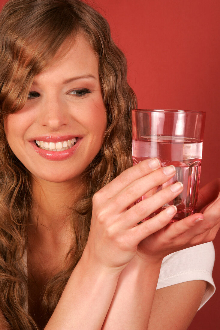 Pretty woman holding glass of water, looking at it and smiling