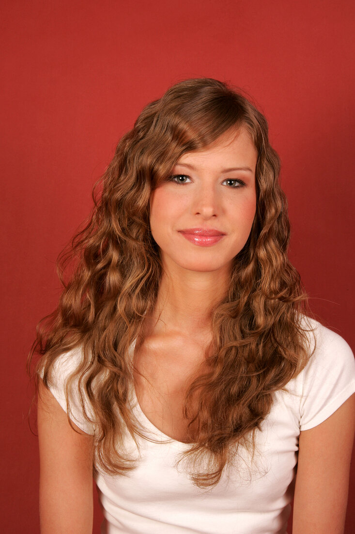 Beautiful woman with long curly hair wearing white top standing and laughing