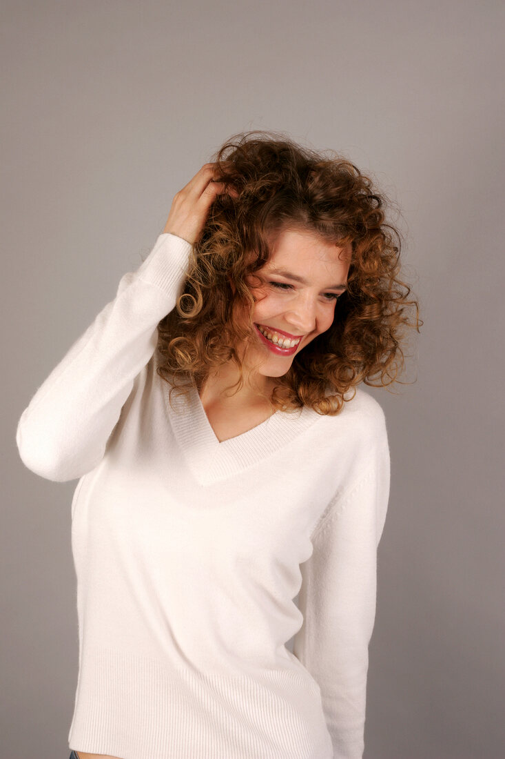 Beautiful woman with curly hair wearing white sweater standing with hand in hair, smiling