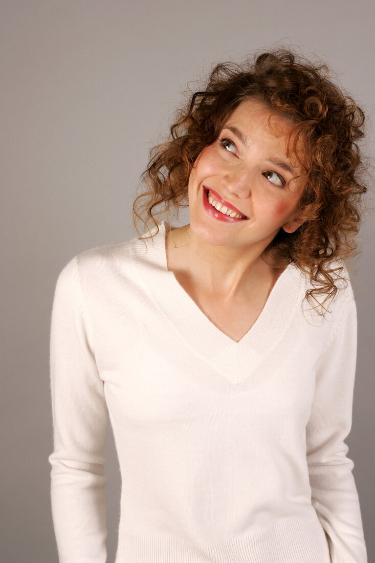 Portrait of happy young woman with curly hair in white sweater, looking up and smiling