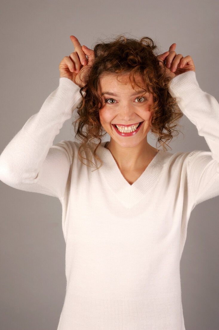 Beautiful woman with curly hair in white sweater making horns with fingers, smiling widely