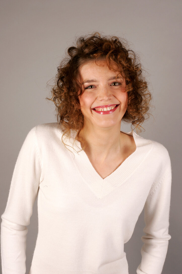 Portrait of happy young woman with curly hair in white sweater, smiling