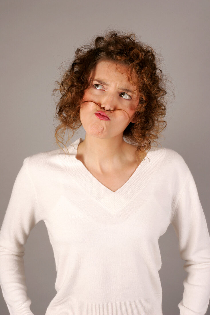 Woman in sweater looking up with strand of hair kept between lips and nose like moustache