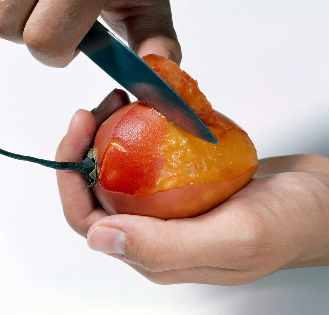 Close-up of hand removing tamarillo skin on white background
