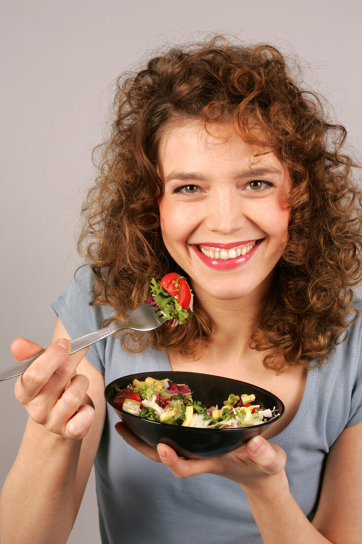 Frau schaut in die Kamera hält Salatschüssel in der Hand