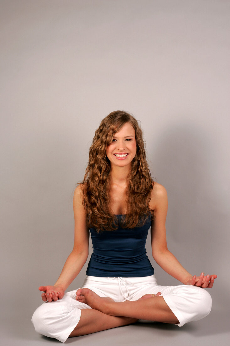 Beautiful woman with long curly hair in blue top sitting and performing yoga