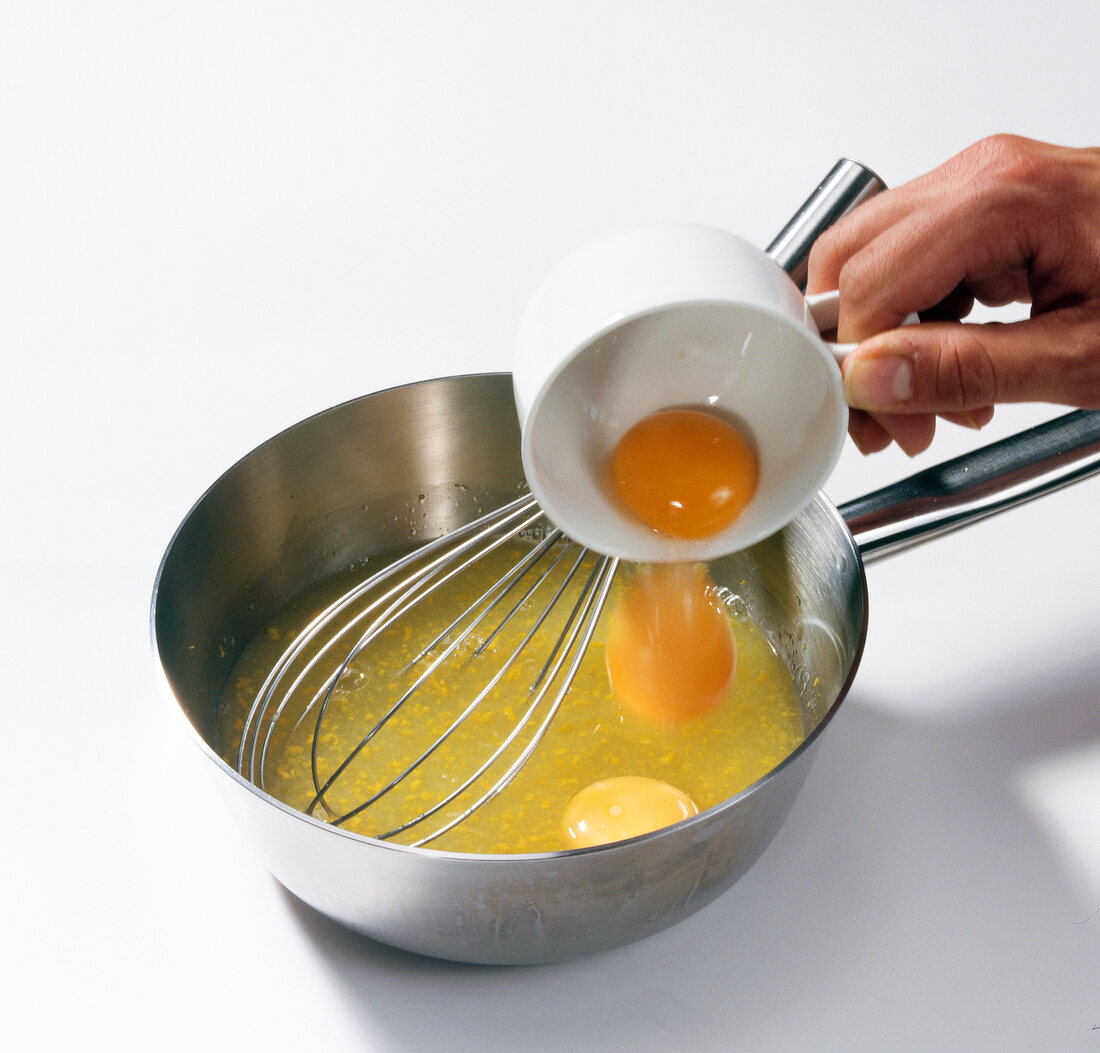 Hand putting egg yolk in pan with whisk