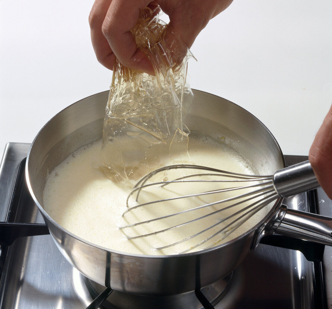 Hand adding gelatine in pot with liquid dough