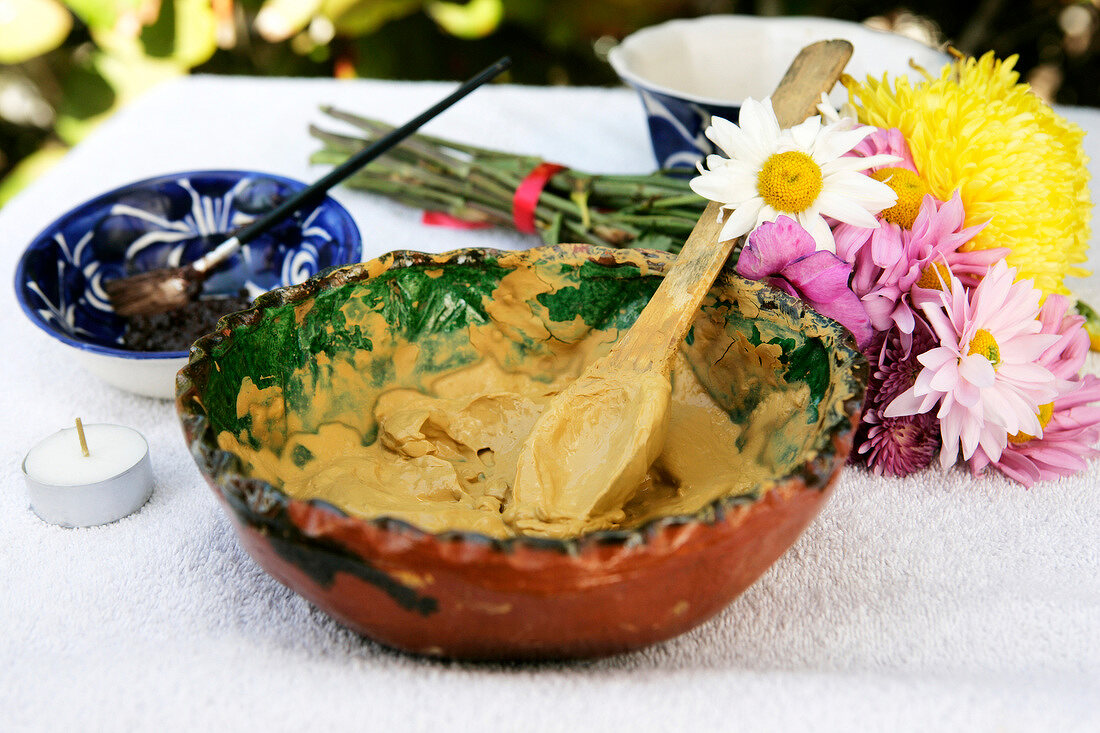 Schale mit Avocado-Körperpackung Holzlöffel und Blüten