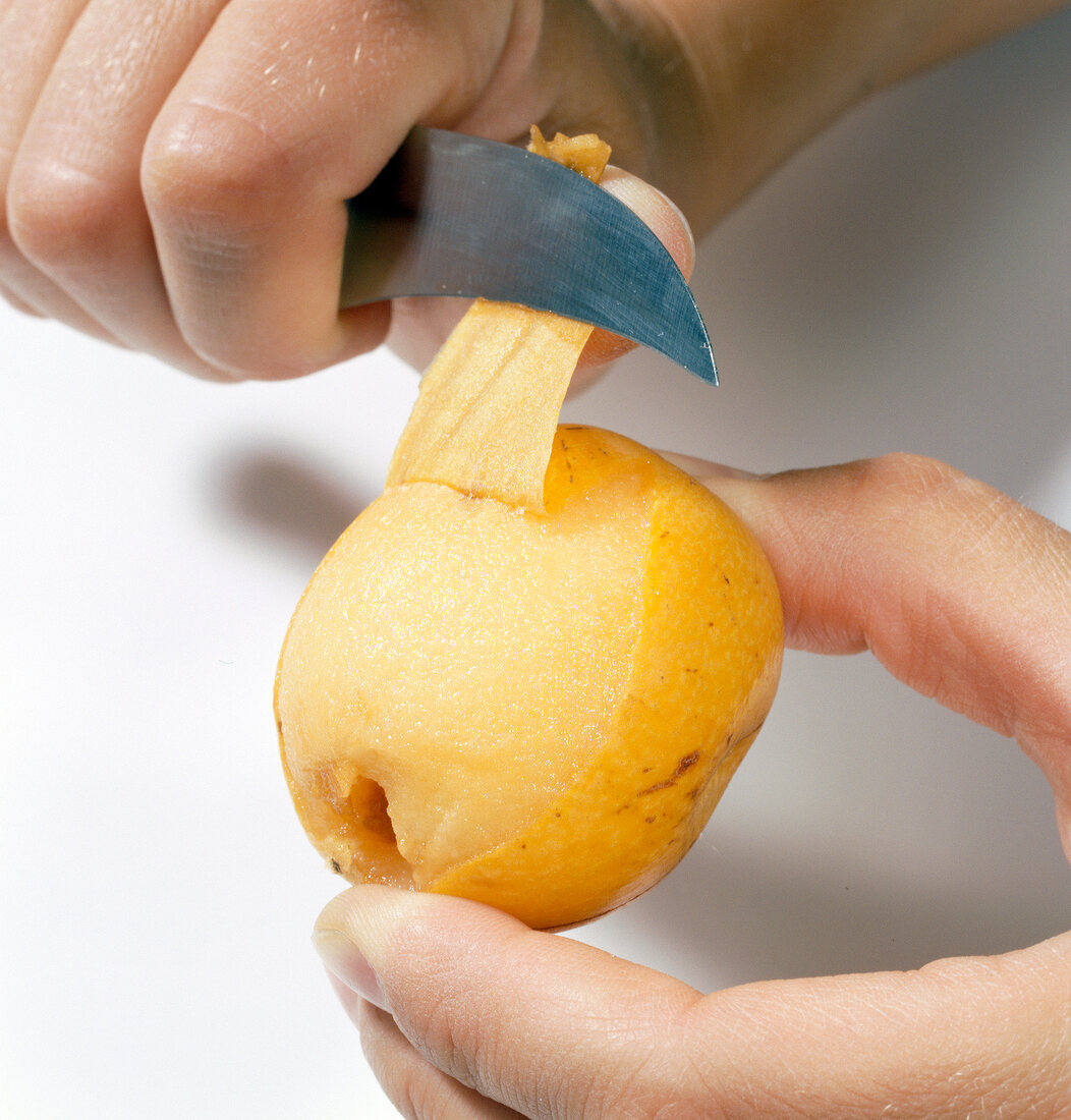 Close-up of hand removing peel of loquat