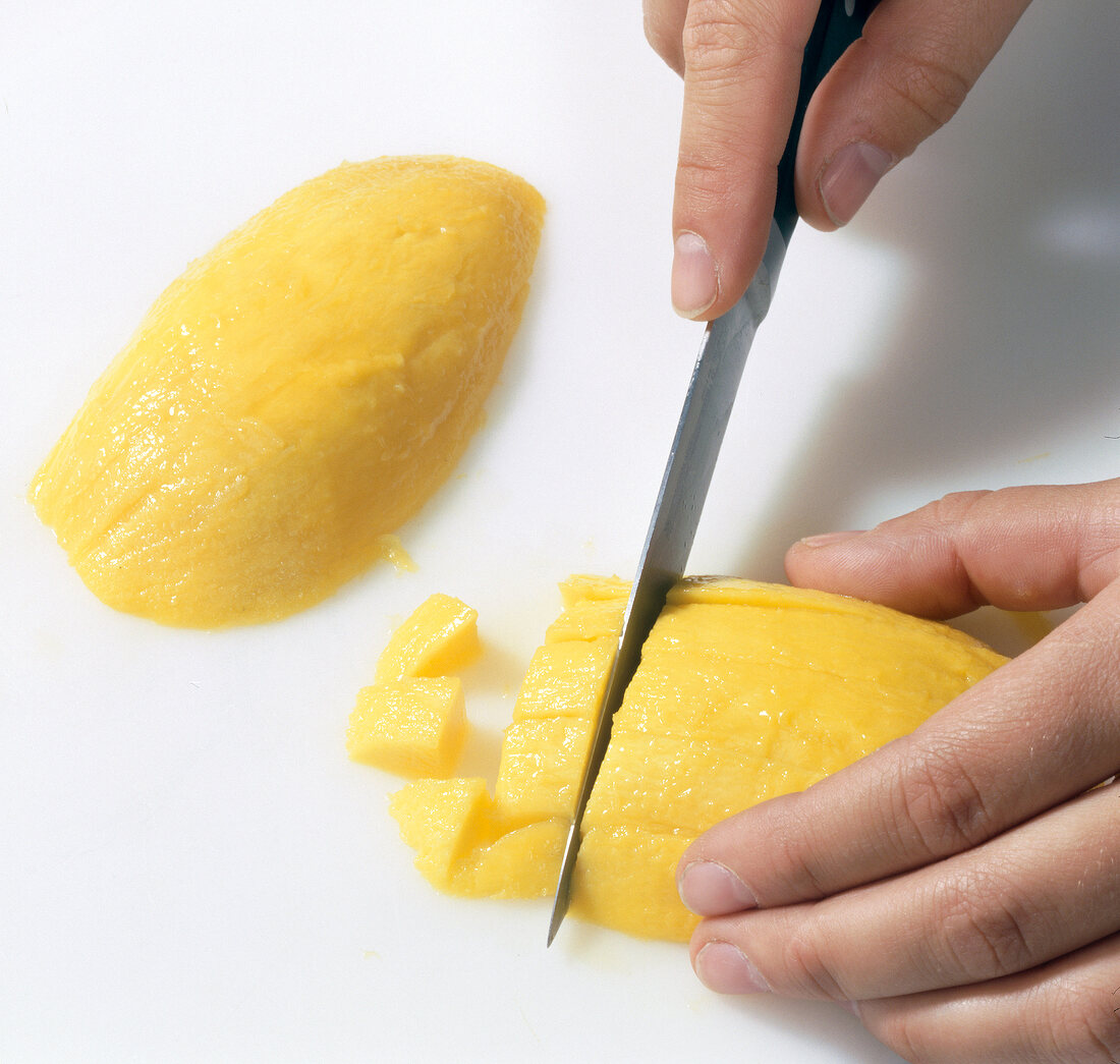 Close-up of hand cutting mango into cubes on white background