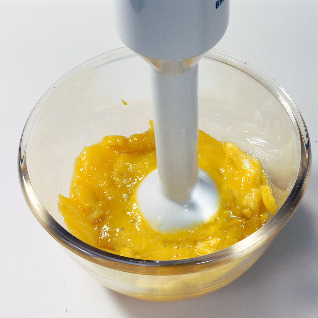 Close-up of hand blending mango pulp with hand blender in bowl